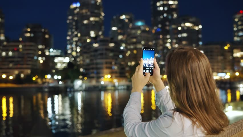 Woman takes pictures of the skyscrapers of Vancouver on her smartphone at night