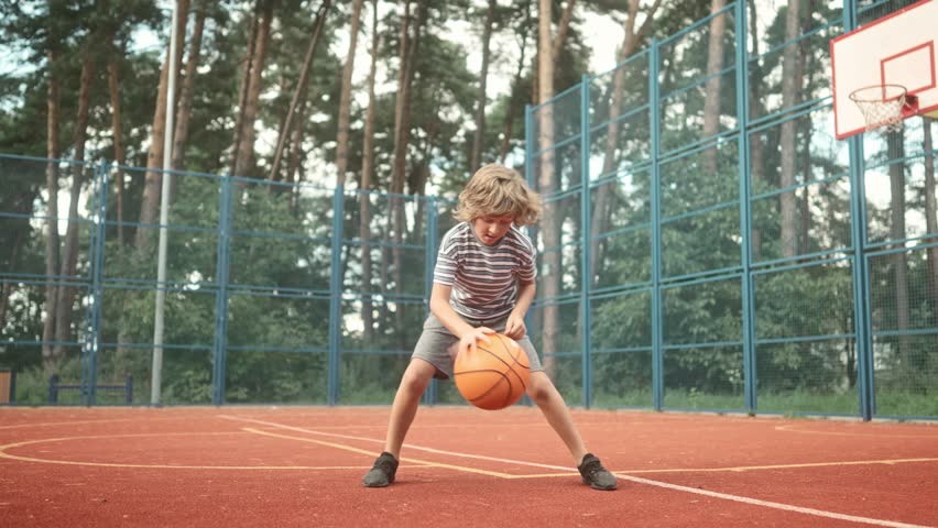 Young boy playing basketball on a court. Little player leading ball and dribbling on court outside. Concept of spending time outdoors, sport activities and happy childhood