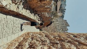 Ancient architecture, woman admiring rock wall under sunny sky. Vertical video