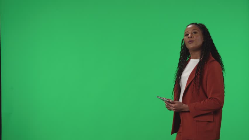 TV Weather Forecast Program. Anchorwoman stands with a tablet in her hands in the studio. African American woman meteorologist pointing at green screen. Advertising area, workspace mock up. Royalty-Free Stock Footage #1105560315