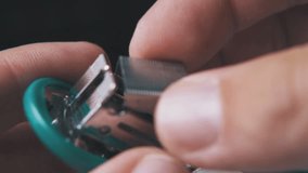 man hands put metal clips into small turquoise stapler on dark background extreme close view