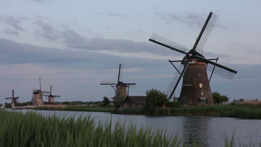 Beautiful wooden windmills at sunset in the Dutch village of Kinderdijk. Windmills run on the wind. The beautiful Dutch canals are filled with water. Beautiful sunset. Royalty-Free Stock Footage #1105567461