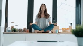 Video of pretty young woman in lotus position sitting on the table while relaxing in the kitchen at home.