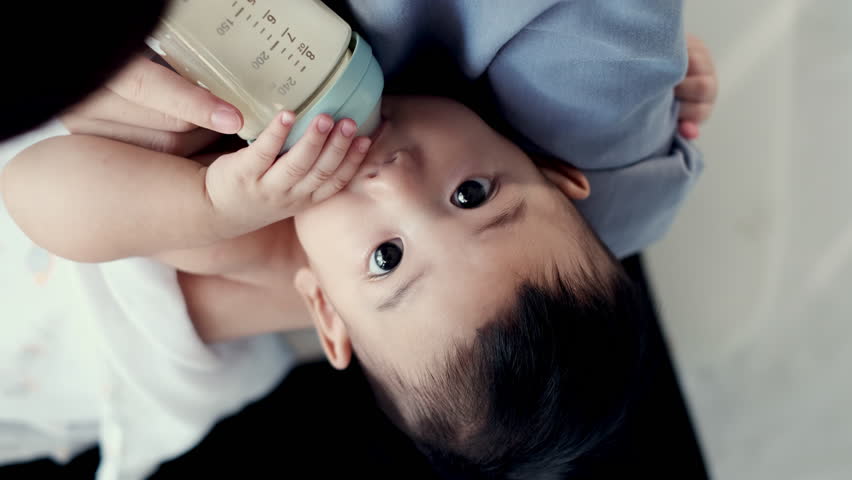 Top view, Adorable little Asian baby looking at camera drinking from baby bottle. Mother holding adorable her son with milk feeding from milk bottle. Concept babies healthcare. Royalty-Free Stock Footage #1105572543
