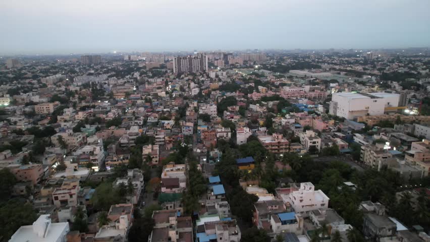 A crowded neighborhood in Chennai City is seen from above in the evening, along with high-rise buildings and metro rail construction.