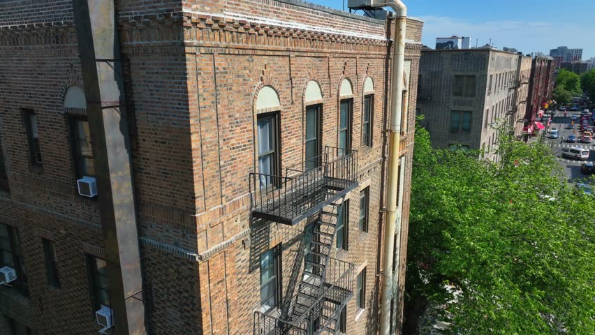 Aerial descending shot of old apartment complex in New York City with fire escape and window air conditioning units in summer.