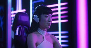 Portrait of a Happy Asian Girl in Headphones Talking with Friends Online on a Computer. Smiling Streamer or Video Gamer Playing Games and Chatting with Internet Followers in a Futuristic Neon Studio