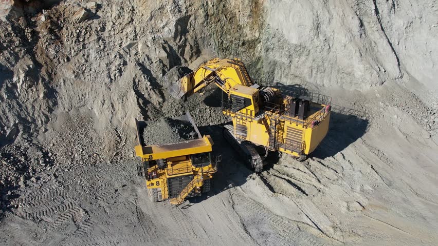 Large bucket excavator loads ore into a large dump truck in open mine gold digging pit, slow motion aerial shot Royalty-Free Stock Footage #1105580639