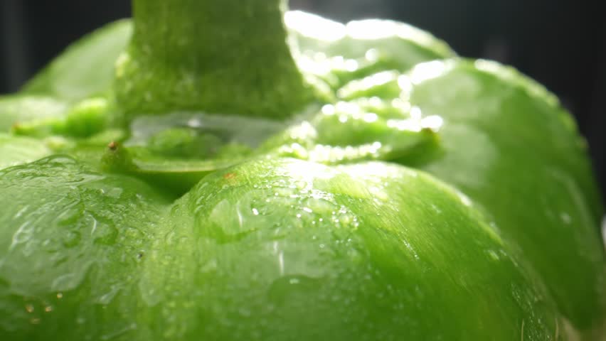 Macro video captures the vibrant green bell peppers glistening with droplets of water. The probe lens reveals intricate details, making it a visually stunning sight. Bell peppers background
