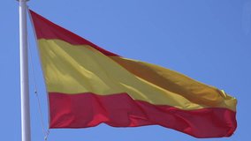 Spain Spanish flag waving in the wind on a flagpole with blue sky background.