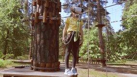 The girl plays a virtual game, she goes in for sports virtually. Virtual reality glasses help in sports. Virtual glasses are immersed in a children's forest rope adventure park.
