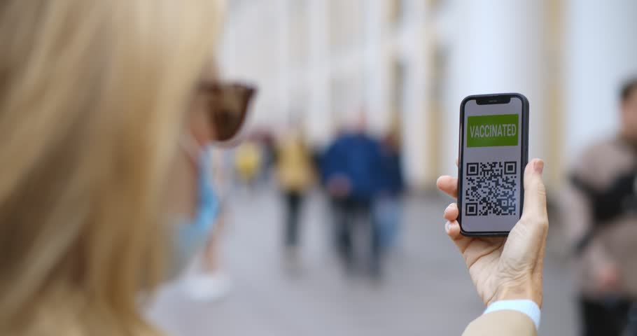 Woman in safety mask holding smartphone with vaccinated qr-code outdoors. Close up of female standing on city street holding cellphone with electronic vaccination certificate | Shutterstock HD Video #1105589113