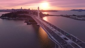 Epic rose golden sunset over San Francisco Bay bridge. Traffic at modern suspension bridge construction from Oakland to San Francisco downtown with scenic sunlight on background. Drone aerial USA 4K