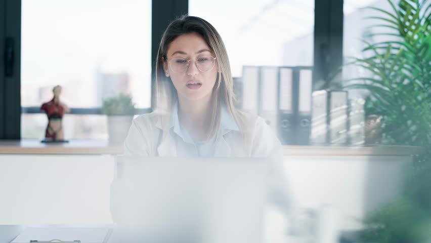 Video of serious female doctor working with her laptop in the medical consultation.