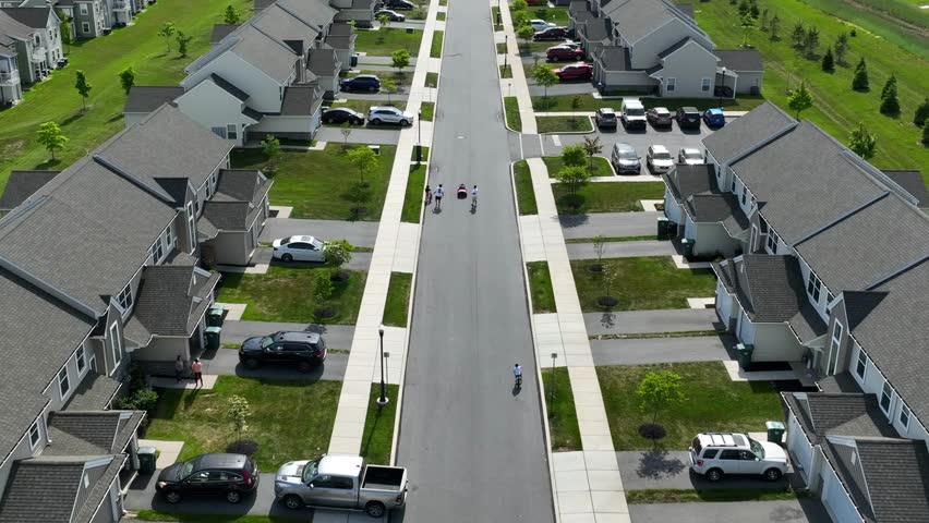 A drone flies over homes in suburban housing development. Aerial dolly forward over family playing outside in the street.