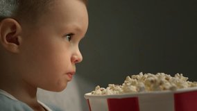Face of attentive child boy eats popcorn and watches cartoon on movie projector.