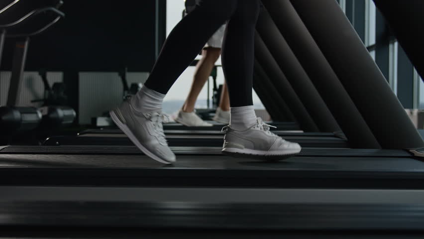 Sporty people jogging on treadmill unknown sportswoman female runner legs feet in sneakers run on sport machine in fitness gym cardio exercise jog fast interval running pace workout healthy lifestyle Royalty-Free Stock Footage #1105603363