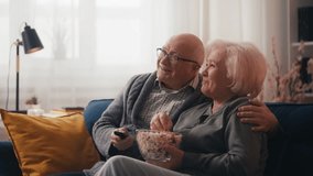 Joyful couple in their 60s watching comedy tv show and laughing, eating popcorn - Powered by Shutterstock - Get 15% off with code: PIKWIZARD15