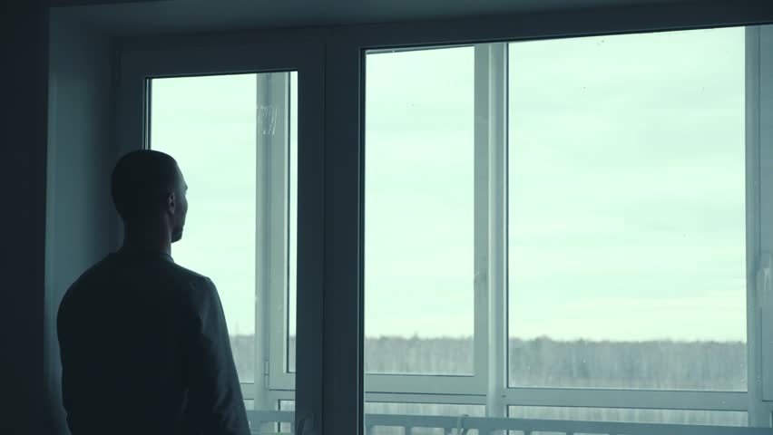A Man Looks Out Of The Window Of His Apartment. Man Looking Out The Window And Making Plans For The Future Royalty-Free Stock Footage #1105612007