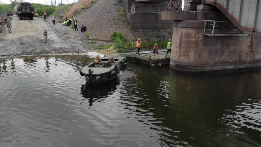 Pontoon bridge of the Ukrainian army. Installation of a temporary crossing near the destroyed bridge. Soldiers collect pontoon ferry. Top view from a drone. 
