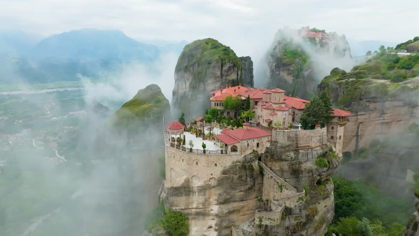Varlaam Meteora Monastery in Greece, rising out of the mist. Amazing mystical panoramic landscape. Epic view of monastery complex on the top of meteora cliffs among clouds and mist. A UNESCO site. Royalty-Free Stock Footage #1105615599