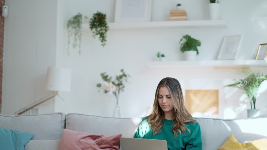 Video of beautiful kind woman working with laptop while sitting on couch in living room at home Royalty-Free Stock Footage #1105620621