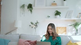 Video of beautiful kind woman working with laptop while sitting on couch in living room at home