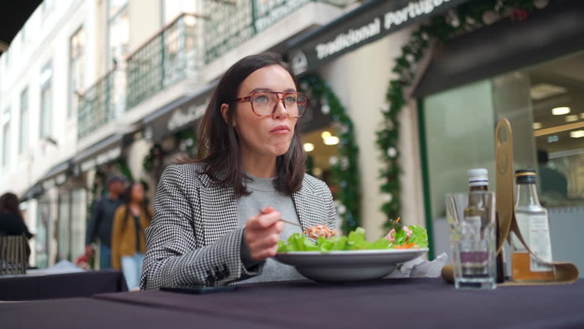 Business lunch. Businesswoman eating salad during lunch break. Caucasian female business person in glasses healthy food in outdoor cafe. Woman eating salad and talking camera sitting in cafe