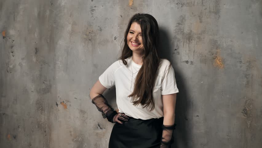Young beautiful woman posing against a gray wall in the studio. Sexy carefree young woman, fashion model
