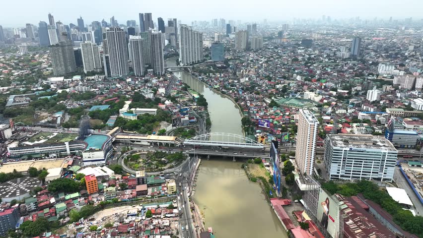 Manila cityscape at river banks aerial. Downtown area with cottages, skyscrapers, buildings. Urban Philippines city scape with streets and roads. Town drone shot. Poor Homes Along Rich Skyscrapers.