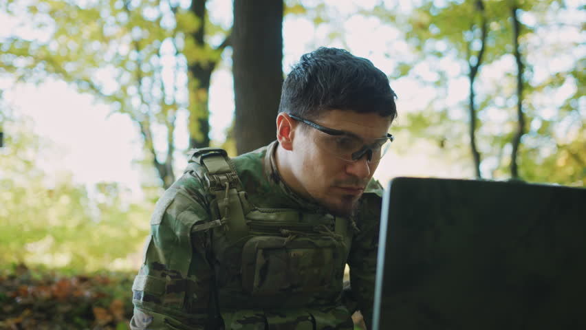 Closeup shot of young focused Caucasian man in special glasses sitting in front of laptop and typing on keyboard. Soldier using computer for drone controlling. Forest. Concept of war Royalty-Free Stock Footage #1105627733