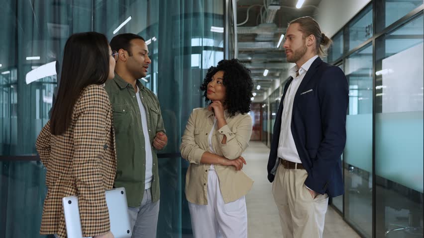 Multinational smiling colleagues talking during break in office hallway