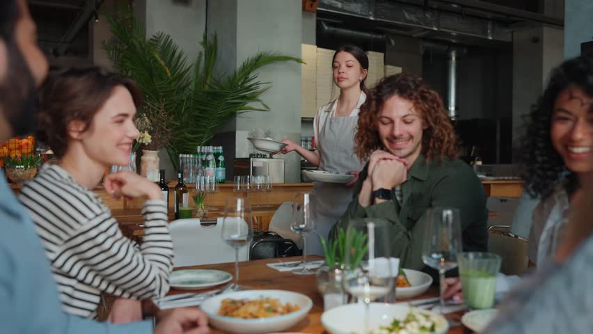 Cheerful waiter brings food to multinational friends celebrating birthday in cafe. Party concept