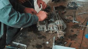 Two mechanics are repairing gearbox on metal workbench. Close-up view of hands of car mechanics. Video 4k. Authentic workflow in car workshop.