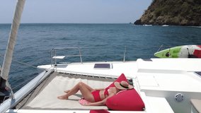 A woman in a red swimsuit is sunbathing on the bow of a yacht, a woman in a red swimsuit is enjoying a trip on a sailing yacht