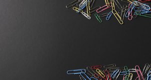 Overhead view of scattered colourful paper clips with copy space on black background, in slow motion. Stationery, learning, school and education concept.