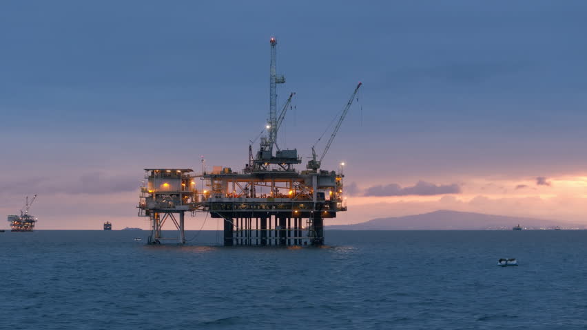Large illuminated oil drilling rig with several ships on the background. USA. Offshore facility for extraction of oil and gas in San Pedro Channel at dawn. High quality 4k footage Royalty-Free Stock Footage #1105635585