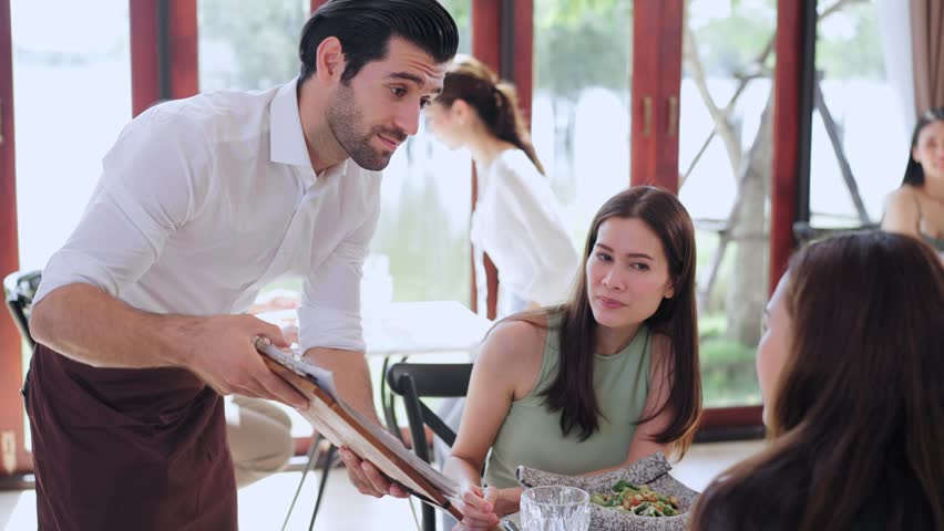 Handsome waiter man suggest food items menu to guest at table in restaurant, Service Food and Restaurant Royalty-Free Stock Footage #1105636979