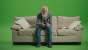 Green Screen. An Old Man With a Gray Beard Plays Computer Games With a Joystick. An Elderly Man Plays PlayStation. Tech Nostalgia and Generational Divide.