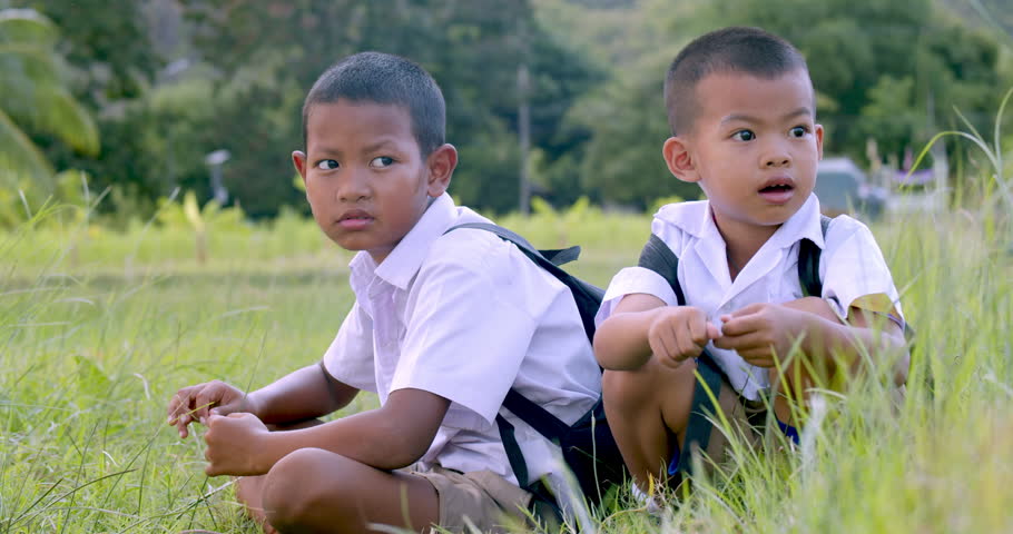 Slow motion : Asian children in white primary school uniform with backpacks which are the sons of poor farmers in rural areas sitting on the path to the school, which had to pass through the fields.