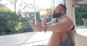 Happy african american man resting making video call using smartphone at sunny home, slow motion. Wellbeing, fitness, communication and healthy lifestyle, unaltered.