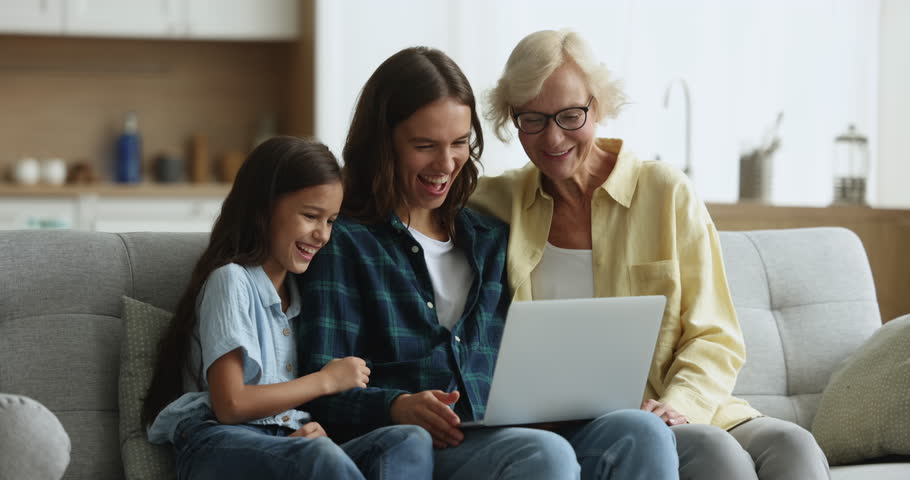 Mature granny spend time with preteen grandchild and millennial daughter laugh while watch funny on-line content, movie via streaming services sit on sofa with laptop. Amusement, family leisure, tech Royalty-Free Stock Footage #1105653565