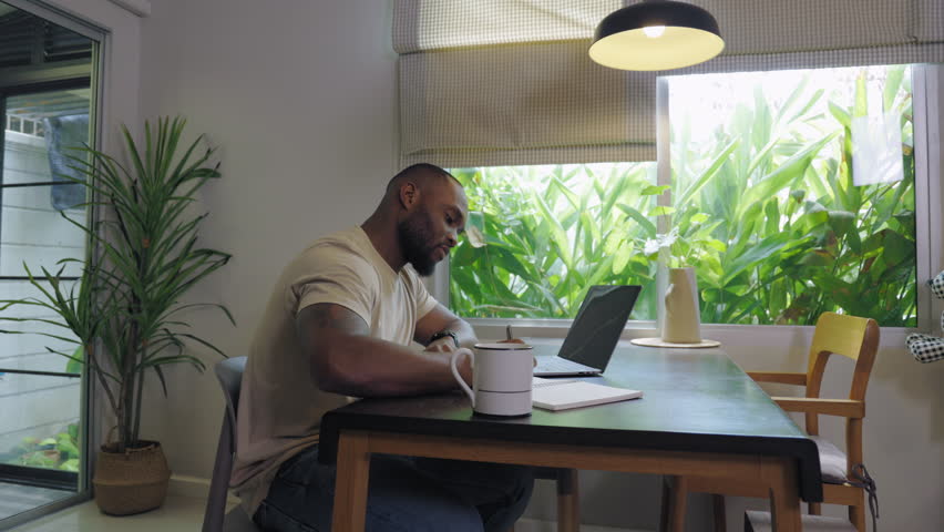 An African male adult studying an online course from his home office. Using a laptop computer, he accesses educational content, takes notes, and actively participates in the class. Royalty-Free Stock Footage #1105654665