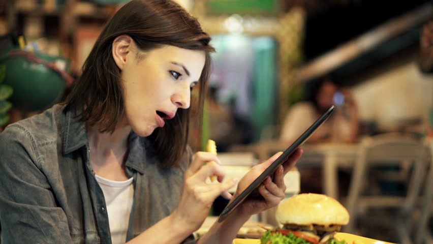 Young woman with tablet computer eating french fries in cafe 
