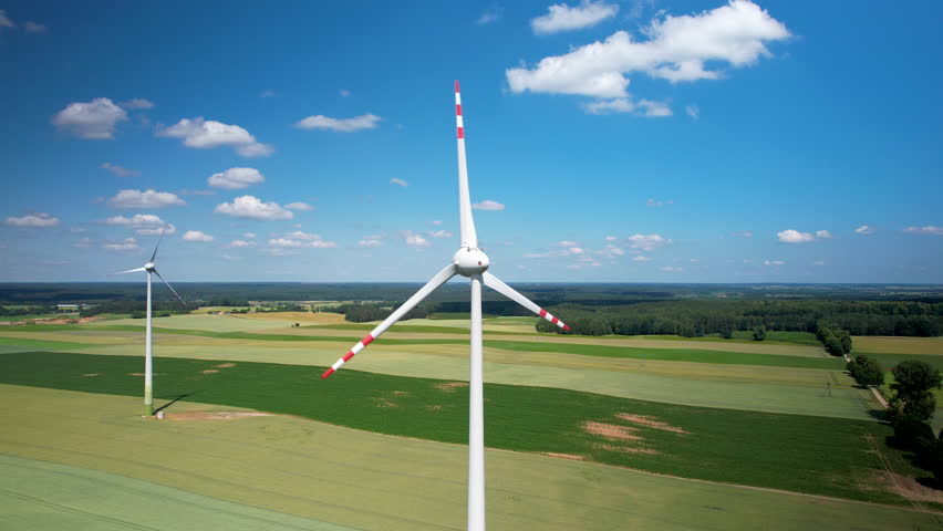 Aerial Close-up Giant Wind Turbine with Rotating Blades in a Vast, Agricultural Field Actively Generating Green Power Energy. Windmill Standing Tall Against Backdrop of the Sky