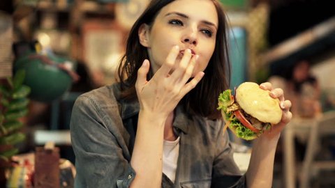 Young woman eating fast food, hamburger and french fries in cafe 
