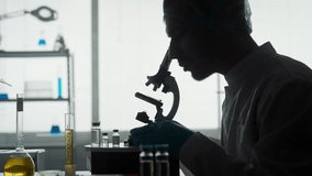 A young scientist in a research laboratory examines a sample on a micropreparation using a microscope. Side view of the dark silhouette of a man sitting in front of a microscope close up. - Powered by Shutterstock - Get 15% off with code: PIKWIZARD15
