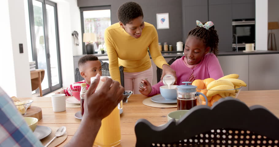 African american parents with son and daughter eating breakfast at table in kitchen, slow motion. Family, food, meal, togetherness, healthy living, lifestyle, and domestic life, unaltered. Royalty-Free Stock Footage #1105667869
