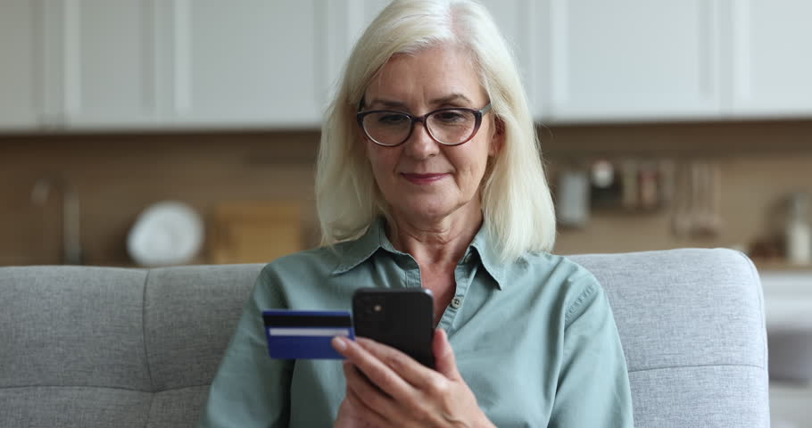 Focused older senior woman in stylish eyeglasses holding banking credit card, typing on smartphone, using modern Internet financial application, making online payment, getting happy, looking away Royalty-Free Stock Footage #1105668371