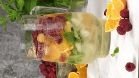 Summer Sangria cocktail or lemonade with raspberry, orange and mint. Refreshing organic non-alcoholic, Detox, healthy drink, fruit in a in a glass decanter. Vertical video, the camera moves forward.